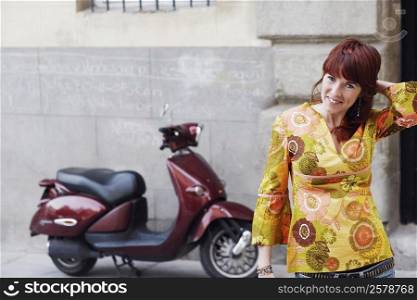 Portrait of a young woman standing in front of a motor scooter
