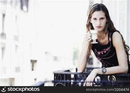 Portrait of a young woman standing in the balcony and holding a glass of coffee