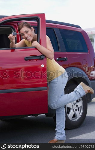 Portrait of a young woman standing near the open door of a car and showing a car key