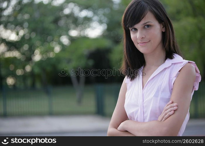 Portrait of a young woman standing with her arms crossed and smirking