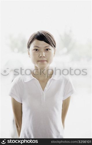 Portrait of a young woman standing with her hands behind her back