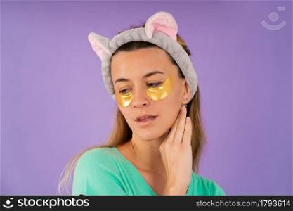 Portrait of a young woman taking care of her skin with under eye patches while standing on isolated background. Beauty and cosmetology concept.