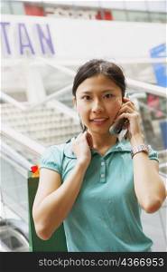 Portrait of a young woman talking on a mobile phone and carrying a shopping bag