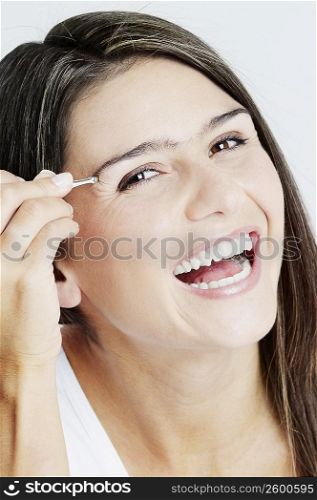 Portrait of a young woman tweezing her eyebrow and laughing