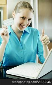 Portrait of a young woman using a laptop and holding a credit card