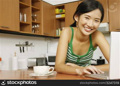 Portrait of a young woman using a laptop at a kitchen counter