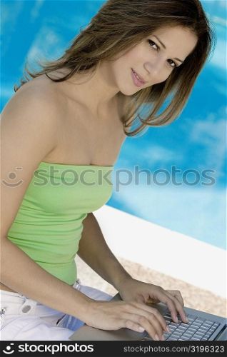 Portrait of a young woman using a laptop at the poolside