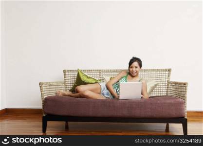 Portrait of a young woman using a laptop on a couch and smiling