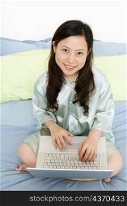 Portrait of a young woman using a laptop on the bed and smiling