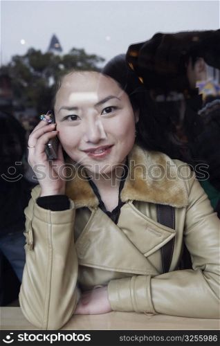 Portrait of a young woman using a mobile phone behind a glass window