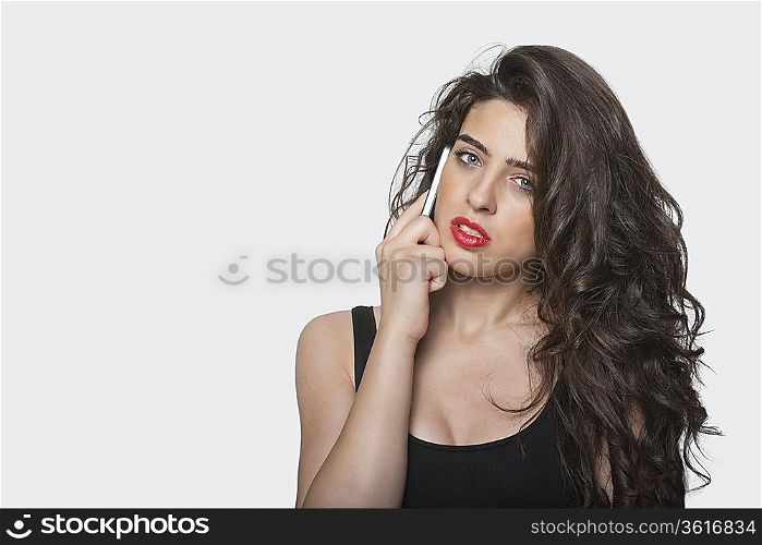 Portrait of a young woman using cell phone over gray background