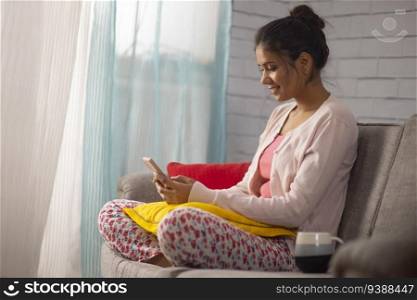 Portrait of a young woman using mobile phone while relaxing on sofa in living room