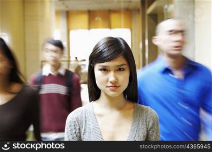 Portrait of a young woman walking in the corridor with three people behind her