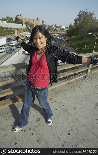 Portrait of a young woman walking on an overpass with her arms outstretched