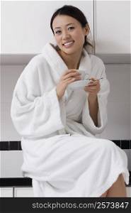 Portrait of a young woman wearing a bathrobe and drinking tea