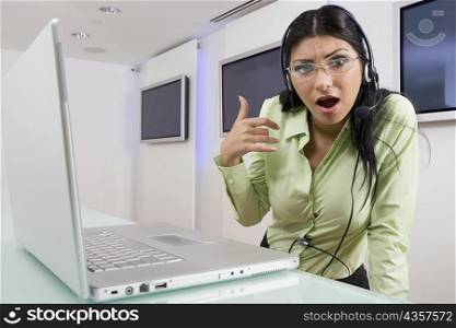Portrait of a young woman wearing a headset and standing in front of a laptop