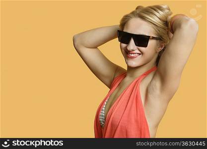 Portrait of a young woman wearing sunglasses with hands in hair over colored background