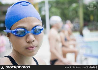 Portrait of a young woman wearing swimming goggles and standing at a poolside