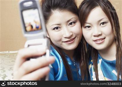 Portrait of a young woman with a teenage girl taking a photograph of themselves