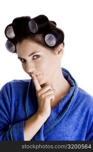 Portrait of a young woman with curlers in her hair and a finger on her lips