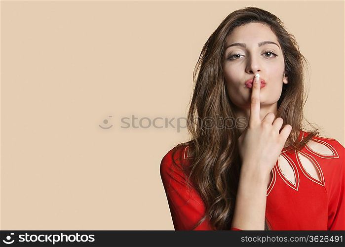 Portrait of a young woman with finger on lips over colored background