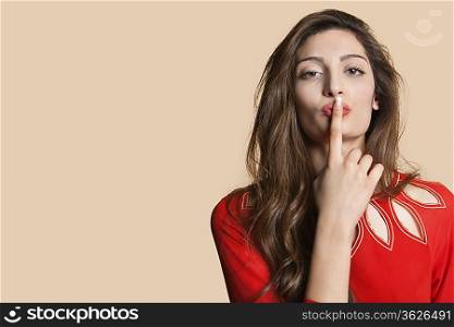 Portrait of a young woman with finger on lips over colored background