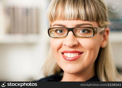 Portrait of a young woman with glasses sitting in front of a book shelf