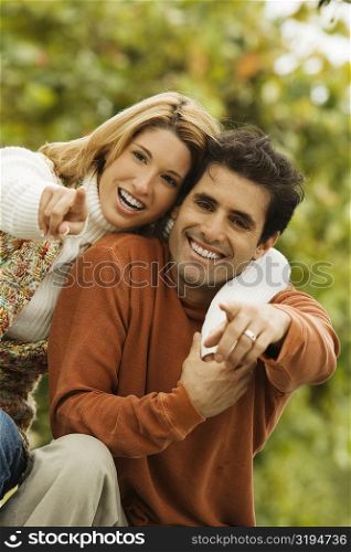 Portrait of a young woman with her arm around a mid adult man pointing forward