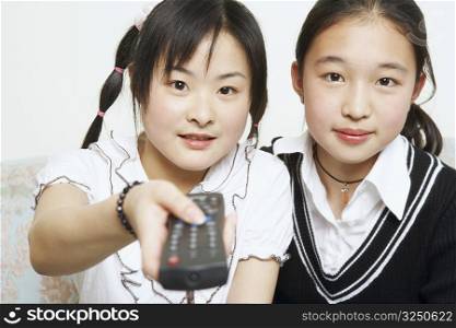 Portrait of a young woman with her sister holding a remote control