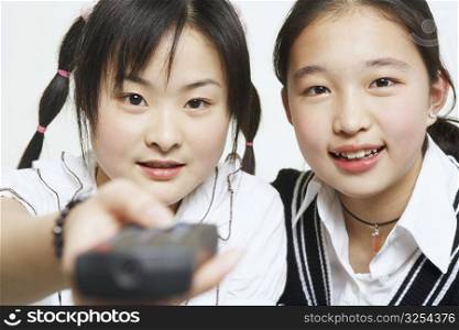 Portrait of a young woman with her sister holding a remote control