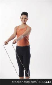 Portrait of a young woman with skipping rope over white background