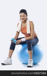 Portrait of a young woman with towel round shoulders sitting on a fitness ball over white background