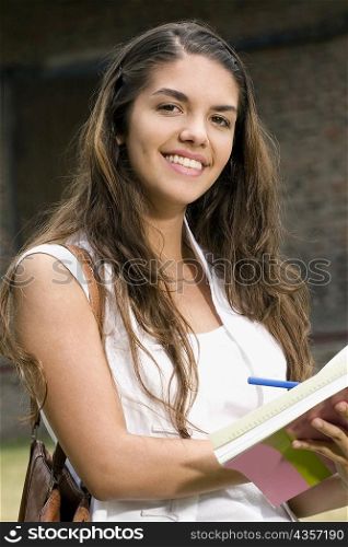 Portrait of a young woman writing in a notepad and smiling