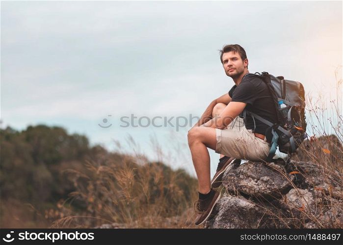Portrait of active Beard man traveler in black shirt sitting and enjoying Breathtaking nature hills scenery on top of mountains. Happy relaxing male with Backpack looking away on the Beautiful landscape. Hiker or climber resting on peak.