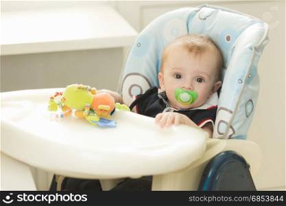 Portrait of adorable 9 months old baby boy with soother sitting in chair