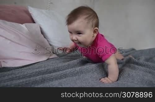 Portrait of adorable baby girl crawling on bed and smiling. Sweet infant child playing, making her first attempts to crawl. Playful little newborn kid enjoying leisure at home. Slow motion.