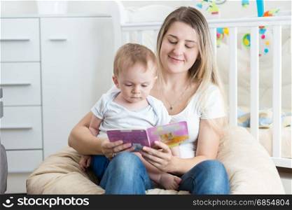 Portrait of adorable baby sitting on mothers lap and reading book