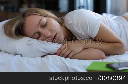 Portrait of adorable blonde female with beautiful long hair snoring while sleeping in bed at home. Closeup. Lovely young woman suffering from snoring. Healthcare concept. Dolly shot.