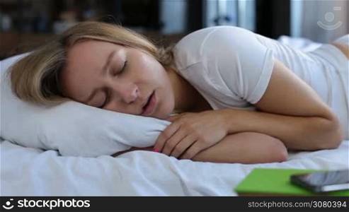 Portrait of adorable blonde female with beautiful long hair snoring while sleeping in bed at home. Closeup. Lovely young woman suffering from snoring. Healthcare concept. Dolly shot.