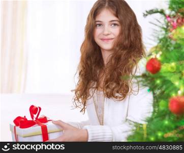 Portrait of adorable girl celebrating New Year at home near Christmas tree, receiving gift box, enjoying festive surprise