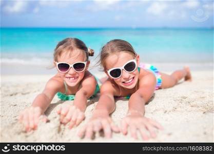 Portrait of adorable little girls having fun on white beach. Close up little girls on sandy beach. Happy kids lying on warm white sandy beach