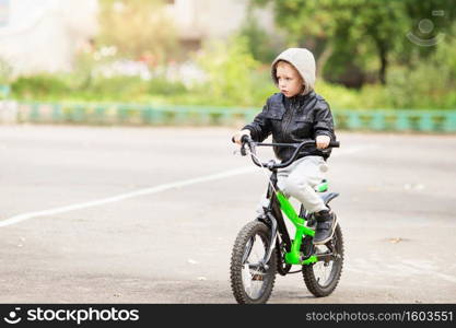 portrait of adorable little urban boy wearing black leather jacket. City style. Urban kids. The boy learns to ride a bike. Child driving a bicycle.