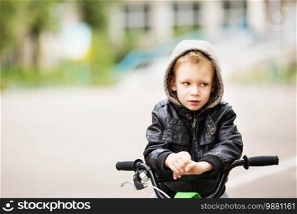 portrait of adorable little urban boy wearing black leather jacket. City style. Urban kids. The boy learns to ride a bike. Child driving a bicycle.