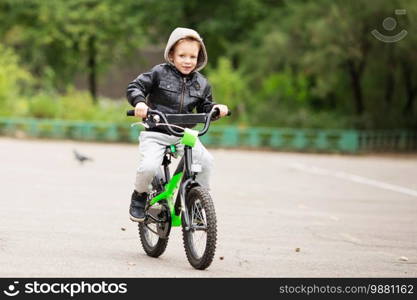 portrait of adorable little urban boy wearing black leather jacket. City style. Urban kids. The boy learns to ride a bike. Child driving a bicycle.