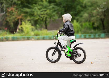 portrait of adorable little urban boy wearing black leather jacket. City style. Urban kids. The boy learns to ride a bike. Child driving a bicycle.