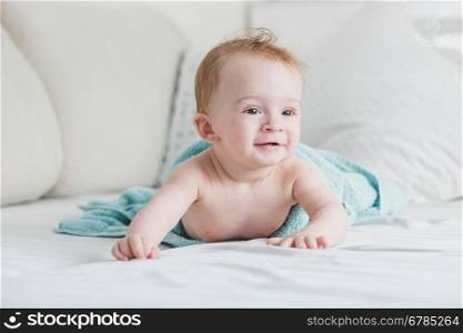 Portrait of adorable smiling baby in blue towel after shower crawling on bed
