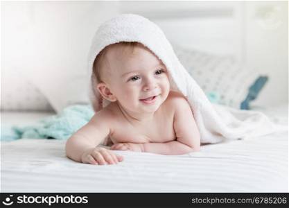 Portrait of adorable smiling baby in hooded towel ling on bed after having bathtime