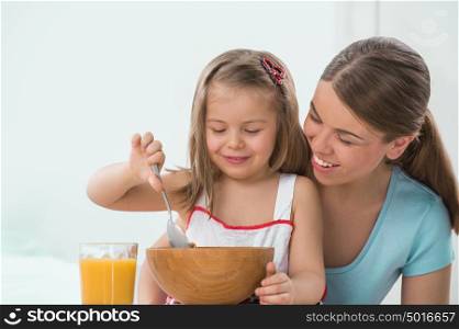 Portrait of adorable young girl and mother in a playful mood having breakfast at home