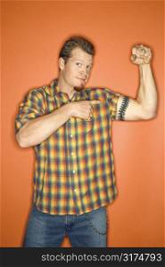 Portrait of adult Caucasian man on orange background flexing and showing off his arm muscle.