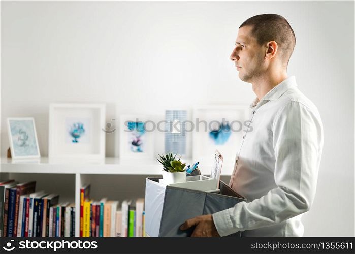 Portrait of adult caucasian man wearing white shirt holding a box personal items stuff leaving the office being fired from work due recession economic crisis downturn losing job company shutdown
